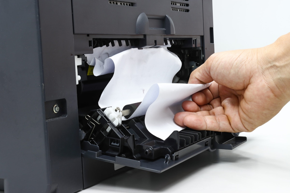 technicians hand removing paper jam from an office copier machine
